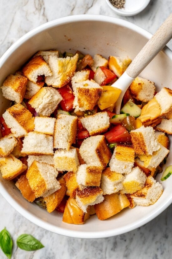 With juicy heirloom tomatoes, crisp cubes of bread, cucumber, and fresh basil, this panzanella recipe is a dish you’ll find yourself making all summer long. Serve it as a side or as a light meal. Stirring bread into bowl of panzanella