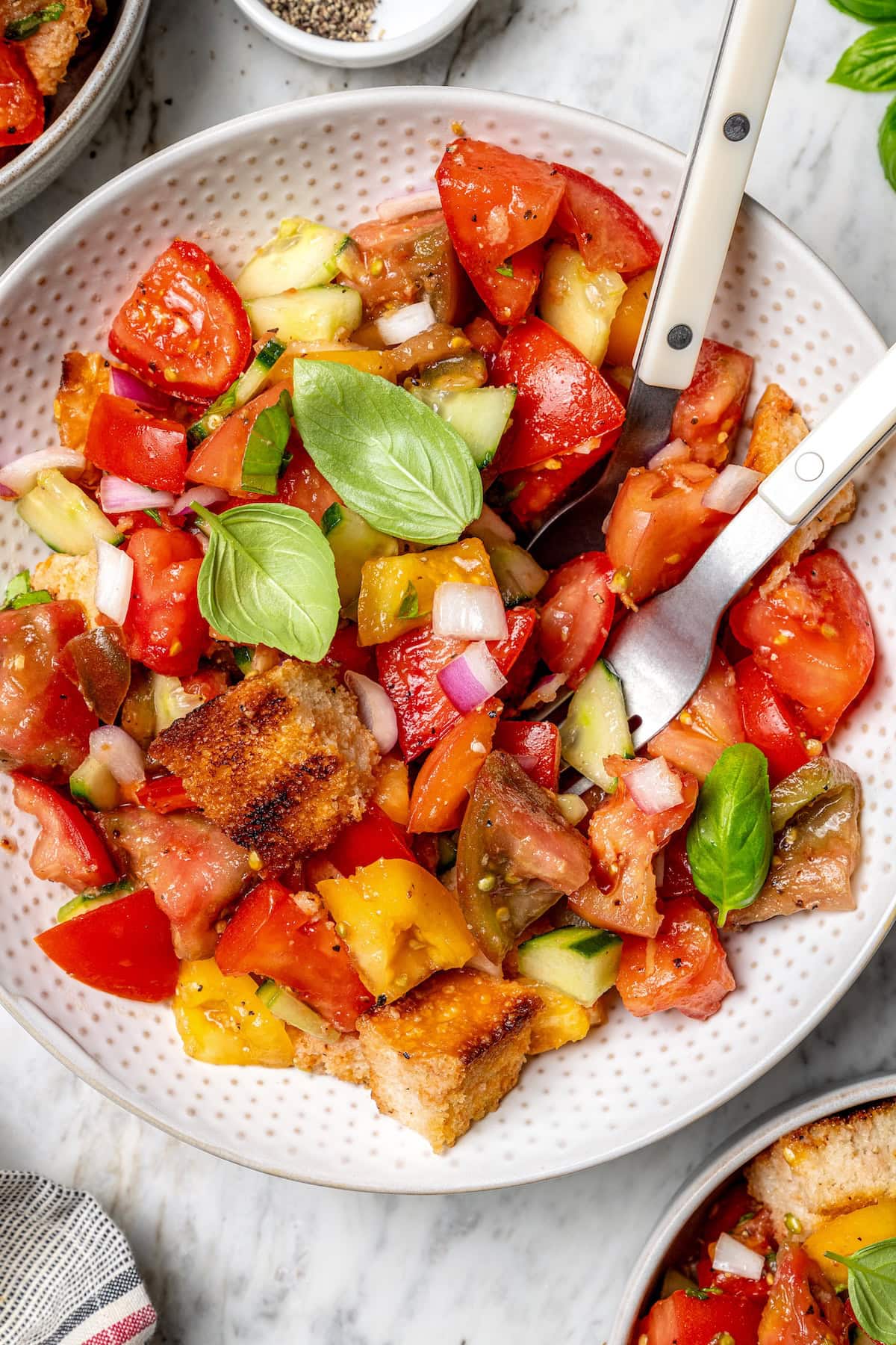 With juicy heirloom tomatoes, crisp cubes of bread, cucumber, and fresh basil, this panzanella recipe is a dish you’ll find yourself making all summer long. Serve it as a side or as a light meal. Overhead view of panzanella salad in bowl with fork and spoon