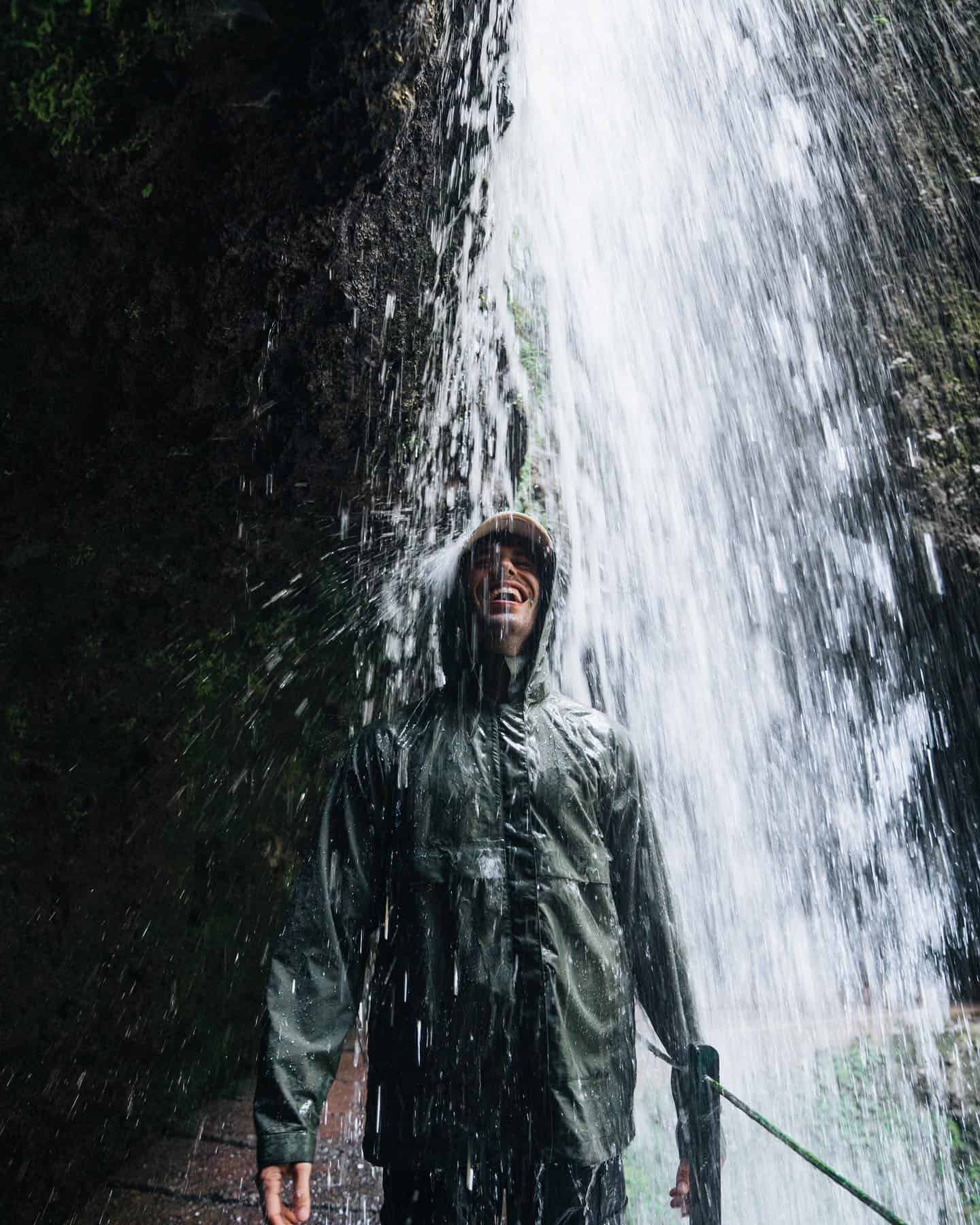 man in a jacket standing under a waterfall