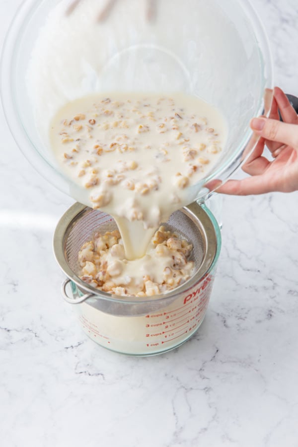 After steeping, pouring the ice cream base through a sieve to strain out the popcorn.