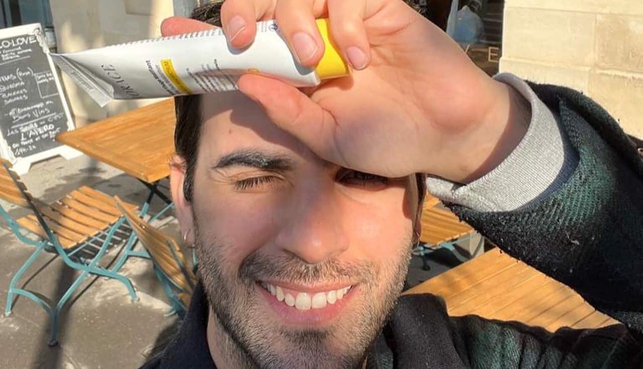 man holding out a tube of horace sunscreen to his for head