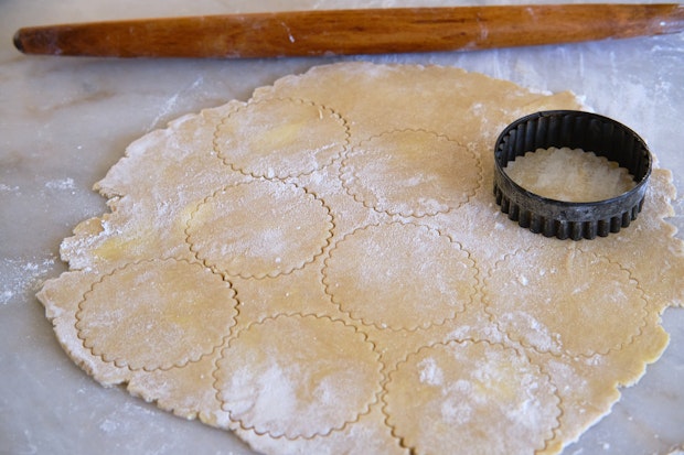 pie dough rolled out on a marble counter with a wood rolling pin