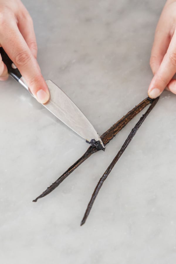 Scraping the seeds out of a split vanilla bean with a paring knife.