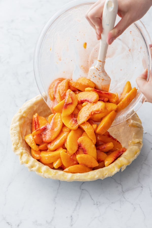 Pouring peach filling into the unbaked pie crust.