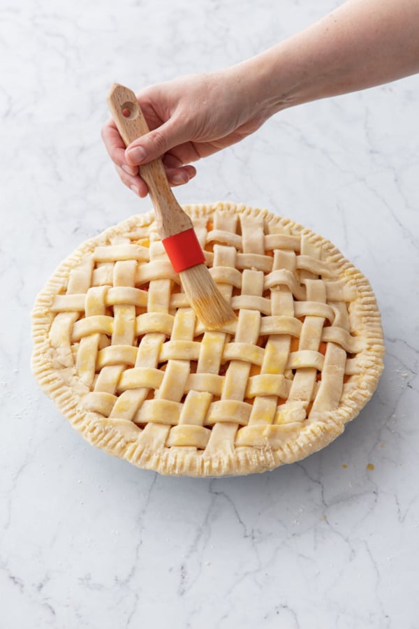 Using a pastry brush to brush the entire top of pie with an egg wash.