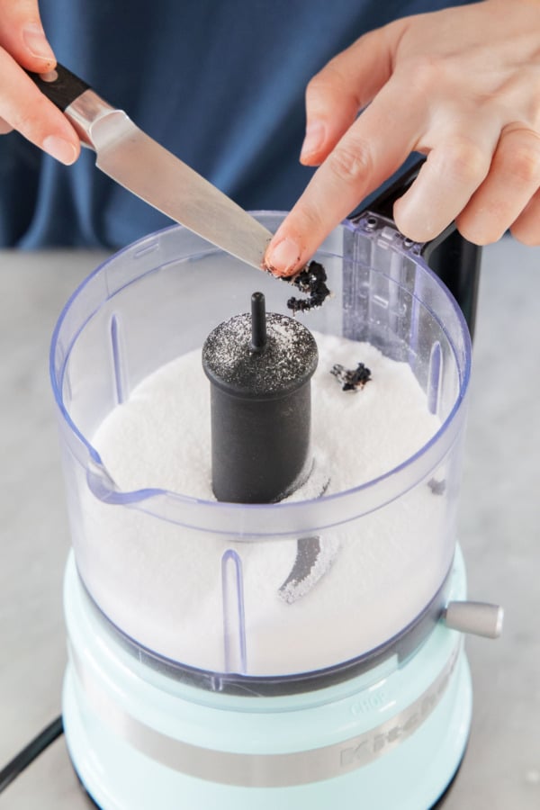 Adding the scraped vanilla bean seeds to a food processor with granulated sugar.