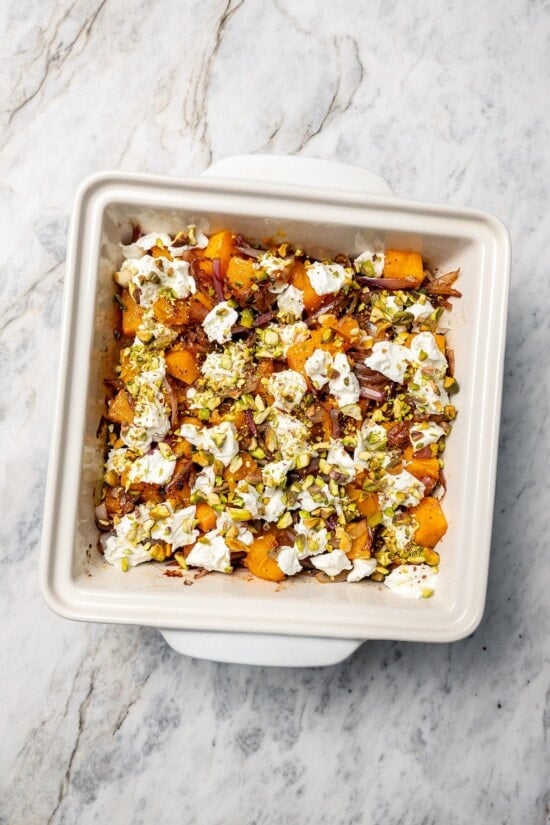 Baked butternut squash is layered with creamy goat cheese, shallots, and pistachios in this cozy side dish recipe. Perfect for the holidays! Baked butternut squash in baking dish with goat cheese, pistachios, and shallots.