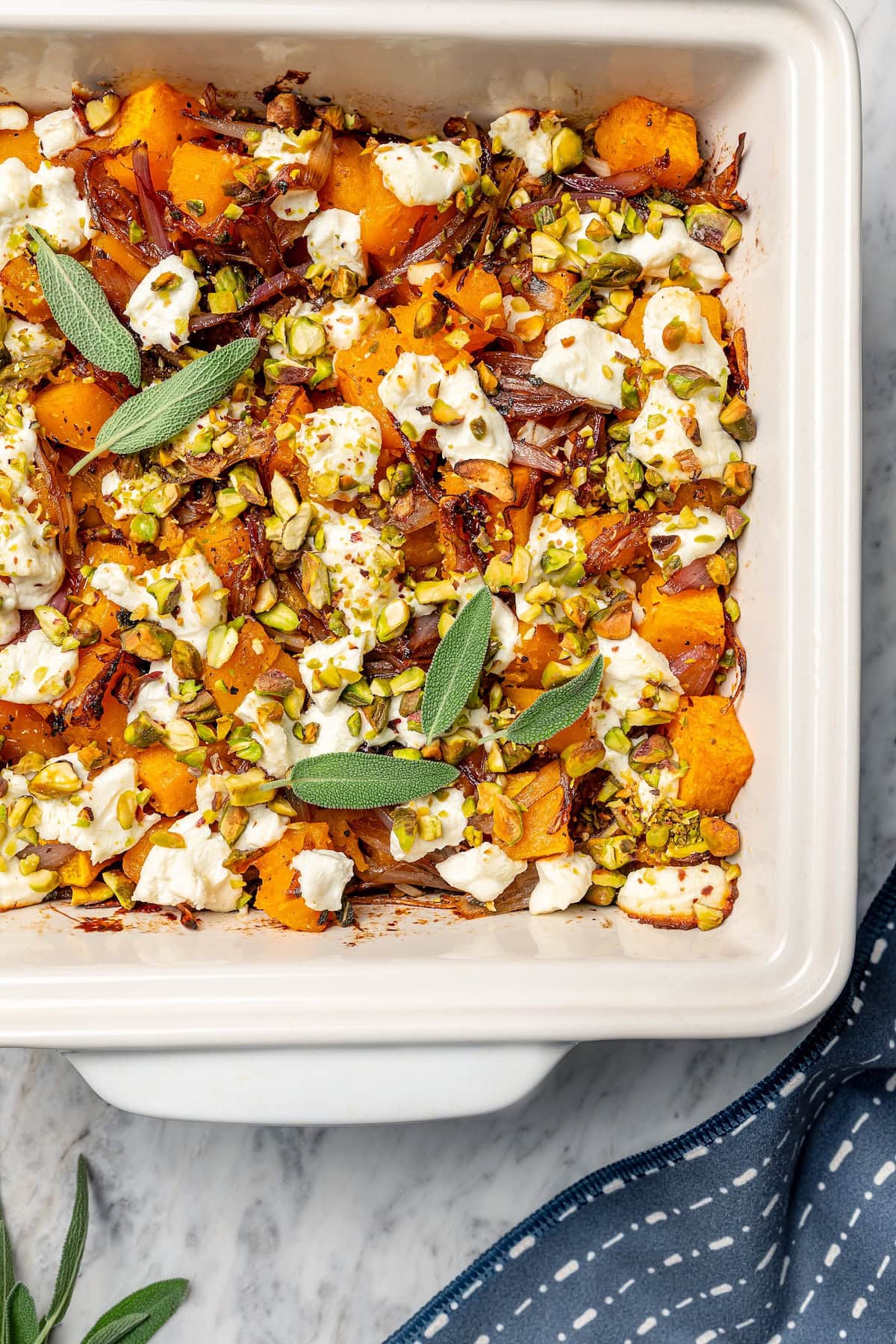Baked butternut squash is layered with creamy goat cheese, shallots, and pistachios in this cozy side dish recipe. Perfect for the holidays! Butternut squash bake in pan
